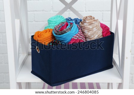 Different scarves in textile box on shelf and white brick wall background