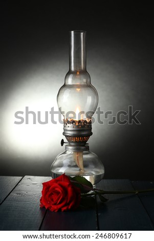 Kerosene lamp with red rose on wooden table on dark lights background