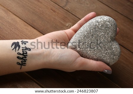 Female arm with tattoo holding decorative heart on wooden background