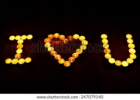 Words I LOVE YOU formed by burning candles on dark background