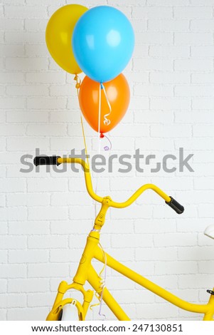 Yellow bicycle with balloons on brick wall background