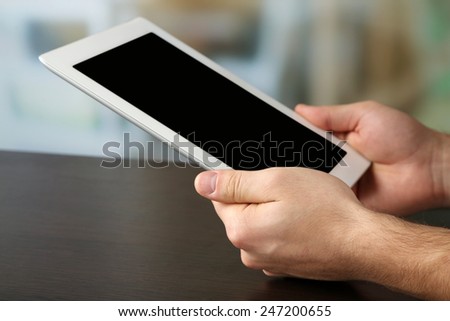 Hand holding Tablet PC on wooden table and light blurred background