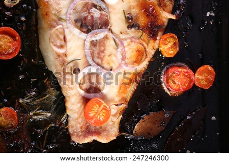 Dish of Pangasius fillet with onion and cherry tomatoes on burn pan background