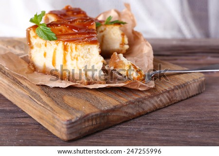 Cheese cake on piece of paper on cutting board on wooden table on curtain background