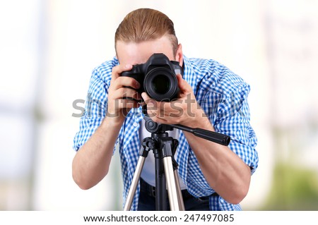 Handsome photographer with camera on tripod indoors