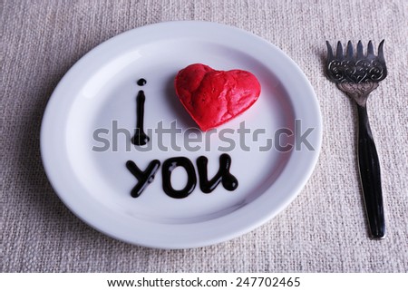Cookie in form of heart on plate with inscription I Love You, on napkin background