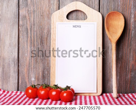 Cutting board with menu sheet of paper, with cherry tomatoes and lettuce on wooden planks background