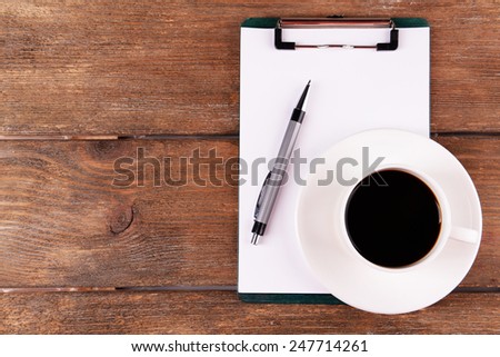 Cup of coffee on saucer with sheet of paper and pen on wooden table background