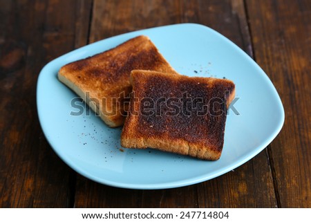 Burnt toast bread on turquoise plate, on wooden table background