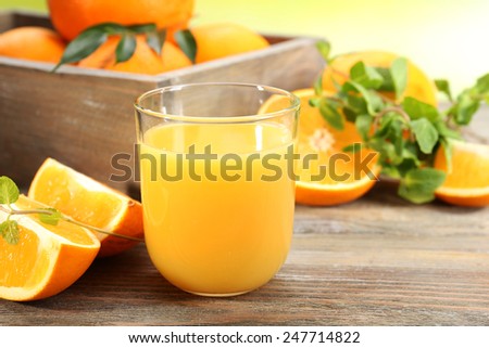 Glass of orange juice with crate of oranges and slices on wooden table and bright background