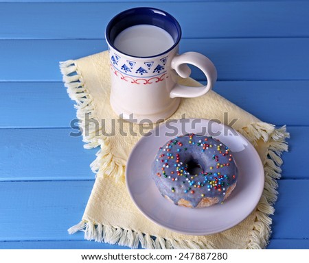 Glazed donut with cup of milk on napkin and color wooden planks background