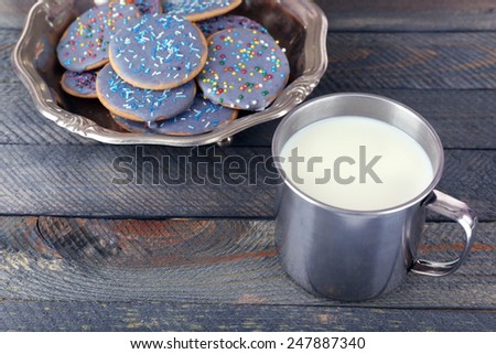 Glazed cookies in metal bowl and mug of milk on rustic wooden planks background