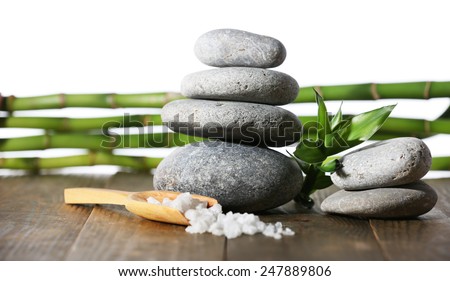 Stack of spa stones with spoon of sea salt on wooden surface isolated on white