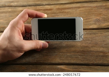 Hand holding smart mobile phone on wooden table background