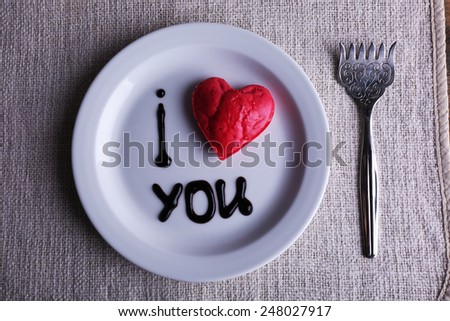 Cookie in form of heart on plate with inscription I Love You, on napkin background