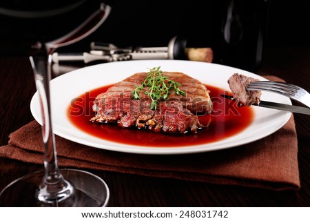 Glass of wine with grilled steak in wine sauce on dark background