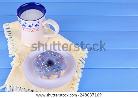 Glazed donut with cup of milk on napkin and color wooden planks background