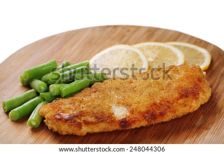 Breaded fried fish fillet and potatoes with asparagus and sliced lemon on wooden cutting board isolated on white