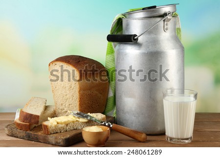 Retro can for milk with fresh bread and glass of milk on wooden table, on bright background. Bio products concept