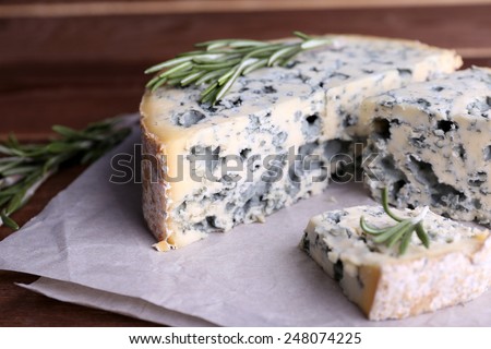 Blue cheese with sprigs of rosemary on sheets of paper and wooden table background