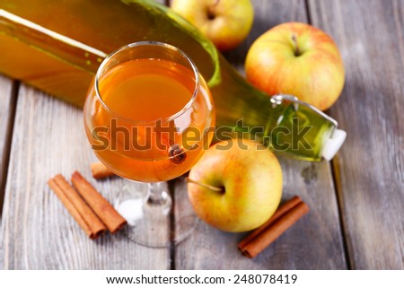 Apple cider in wine glass and bottle, with cinnamon sticks and fresh apples on wooden background