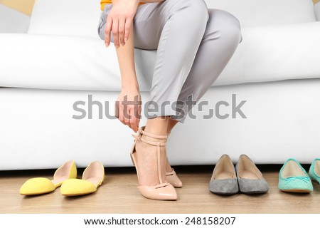 Trying on shoes by elegant lady sitting on white sofa background