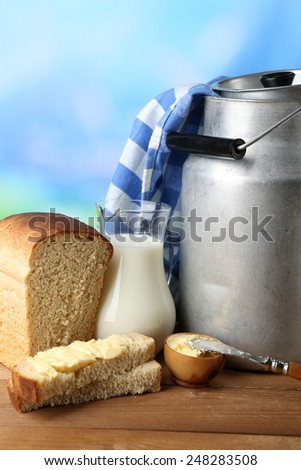 Retro can for milk with fresh bread and jug of milk on wooden table, on bright background. Bio products concept