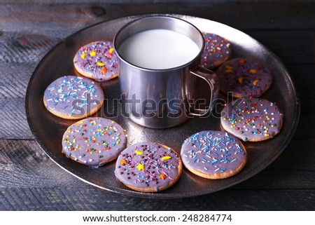 Glazed cookies on metal tray with mug of milk on rustic wooden planks background
