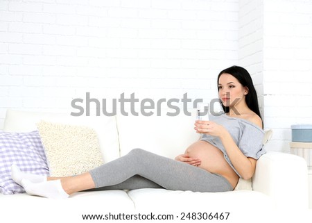 Young pregnant woman relaxing on sofa with glass of water on home interior background