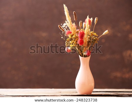 Bouquet of dried flowers in vase on color background