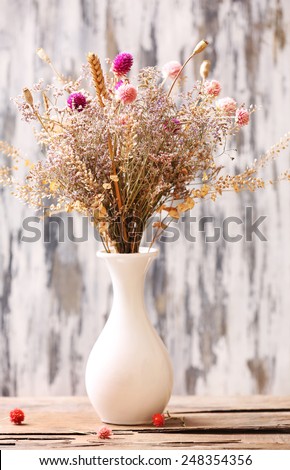 Bouquet of dried flowers in vase on bright background