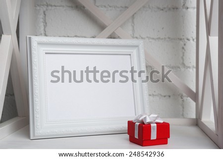 Photo frame with present box on shelf, on brick wall background