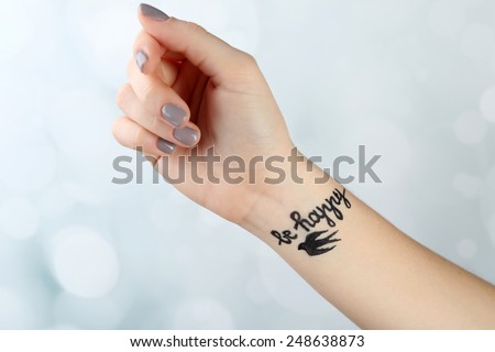 Female arm with tattoo on light background