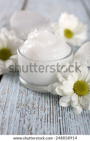 Cosmetic cream with flowers and spa stones on wooden background