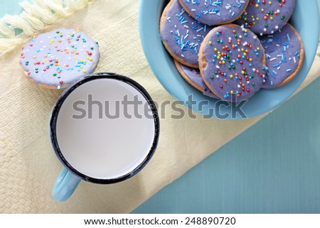 Plate of glazed cookies and mug of milk on napkin and color wooden table background