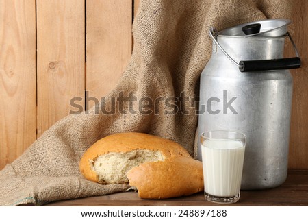 Retro can for milk with fresh bread and glass of milk on wooden background. Bio products concept