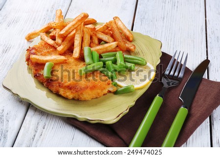 Breaded fried fish fillets and potatoes with asparagus and sliced lemon on plate and wooden planks background