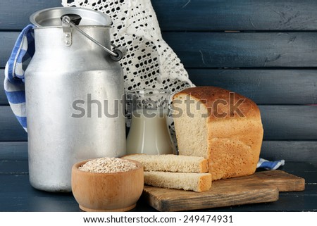Retro can for milk with fresh bread and glass jug of milk on wooden background. Bio products concept