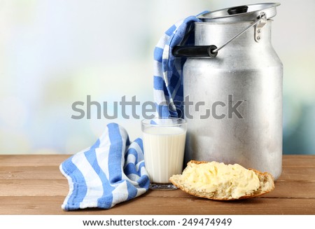 Retro can for milk with fresh bread and glass of milk on wooden table, on light background. Bio products concept