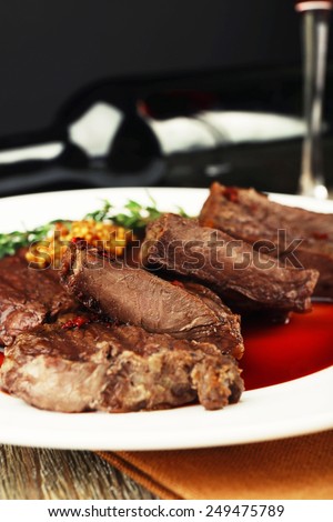 Steak with wine sauce on plate and bottle of wine on dark background
