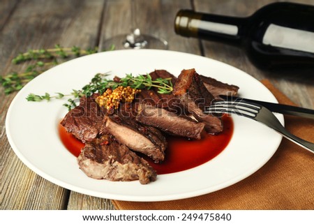 Steak on plate with bottle of wine on wooden background
