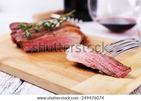 Steak with herbs on wooden stand and wine on table close up