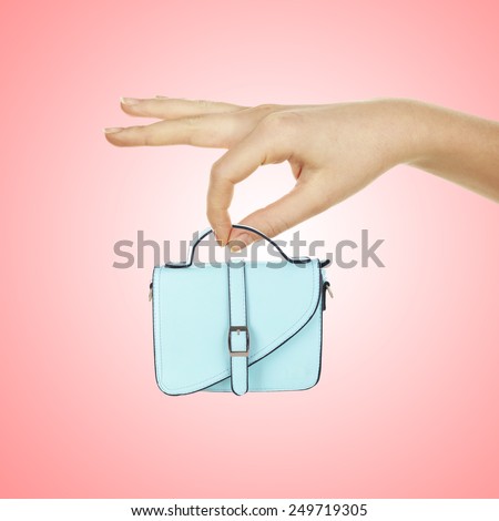 Small female handbag in big hand on light pink background