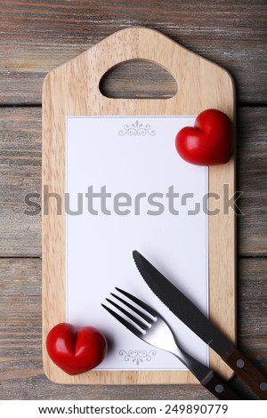 Cutting board with menu sheet of paper and hearts on rustic wooden planks background