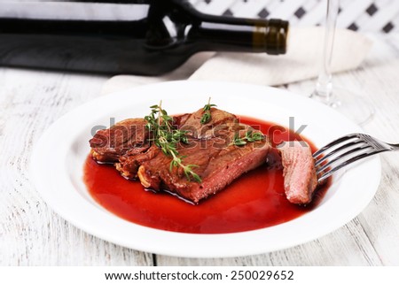 Steak with wine sauce on plate with bottle of wine on wooden background