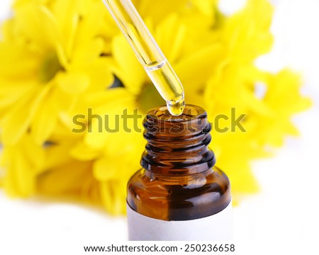 Dropper bottle of perfume with yellow chamomile on white background