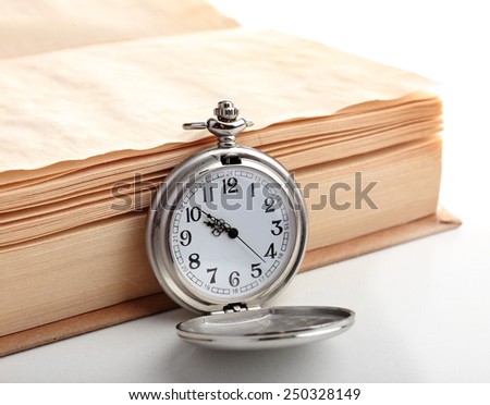 Silver pocket clock and book on white table