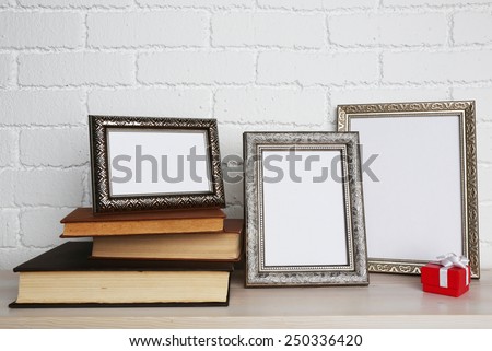 Golden photo frames with books and present box on wooden surface, on brick wall background