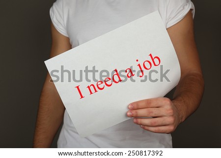Sheet of paper with inscription I need a job in male hand on dark background