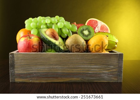 Assortment of fruits in box on dark yellow background